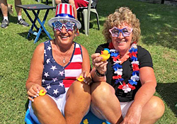 Two campers in stars-and-stripes outfits and novelty sunglasses holding rubber ducks on the grass