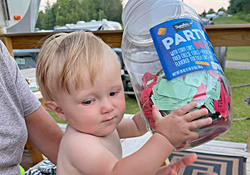 A toddler holding up a clear jar packed full of raffle tickets