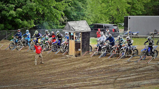 Riders lined up on the gate at the Rider Hill motocross start, an official raising the board