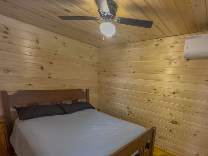 The bedroom with a made bed, a ceiling fan and a wall air conditioner