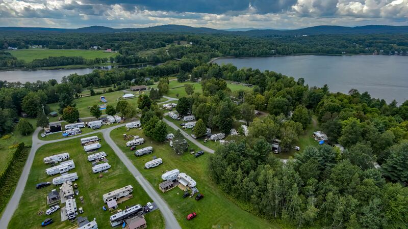 Aerial view of the campground spread across its hilltop, with a lake and distant mountains beyond