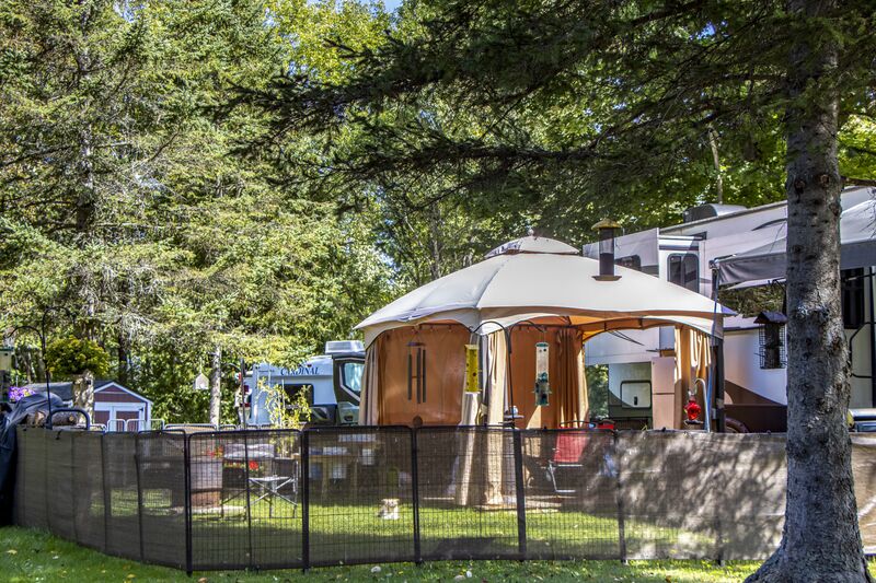 A gazebo and fenced dog run beside a camper at the edge of the trees