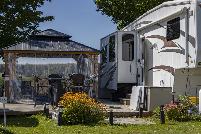 A camper with a gazebo on a wooden deck and beds of orange flowers