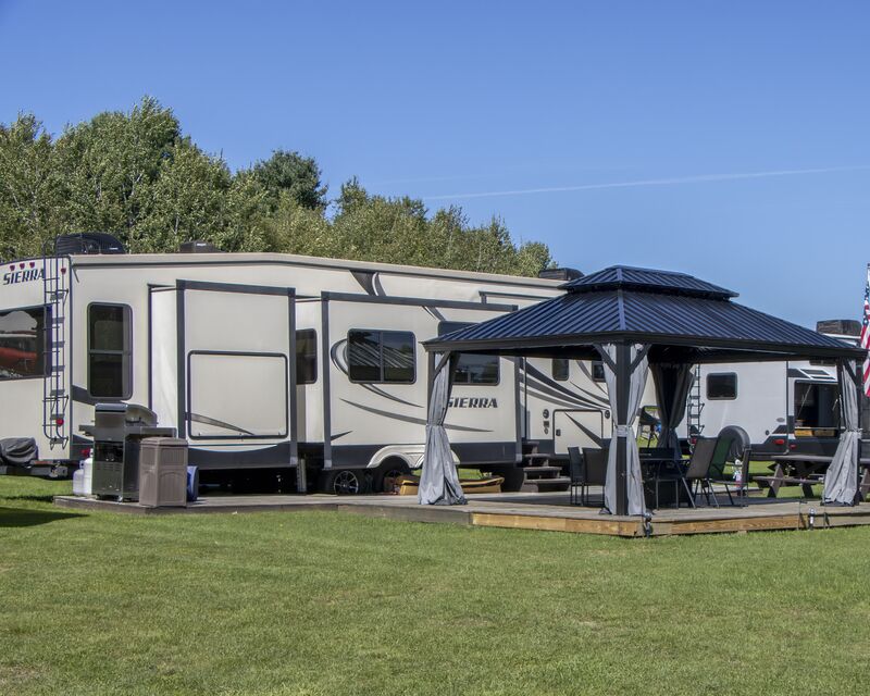 A large fifth-wheel and a hard-topped gazebo on an open, level lawn site