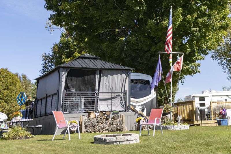 A camper with a screened gazebo, flags and red chairs on a stone-edged site