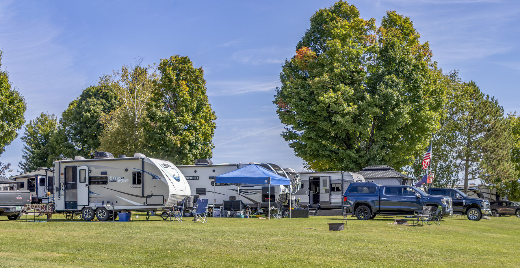Travel trailers parked on wide open grass sites under a clear blue sky with maples turning colour