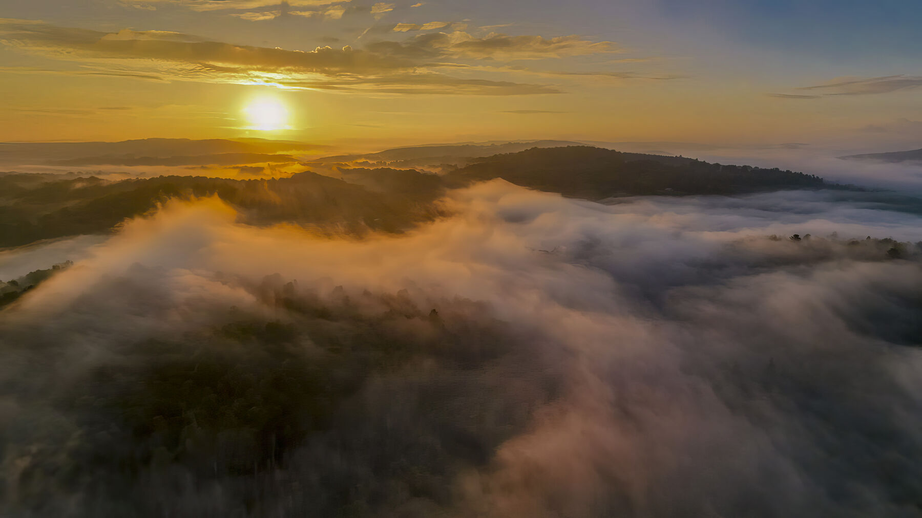 Aerial view at sunrise, the sun low over the hills and fog filling the valleys below