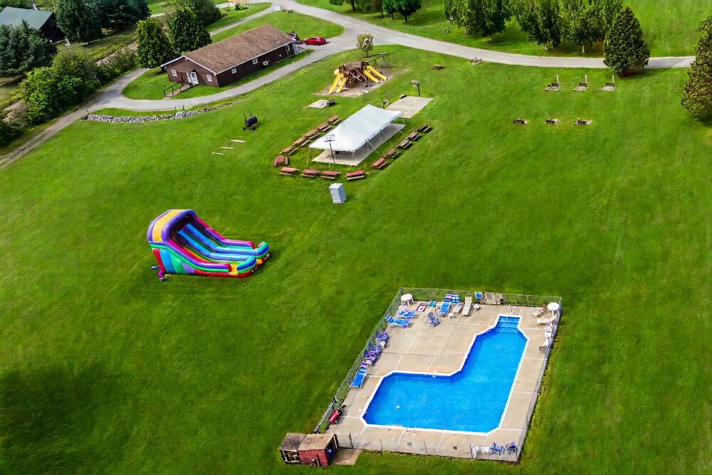 Aerial view of the in-ground pool, a large inflatable slide and the playground on the open field
