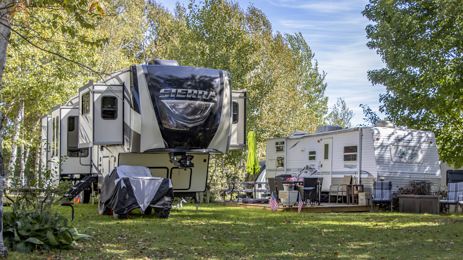 A fifth-wheel and travel trailer nestled among trees