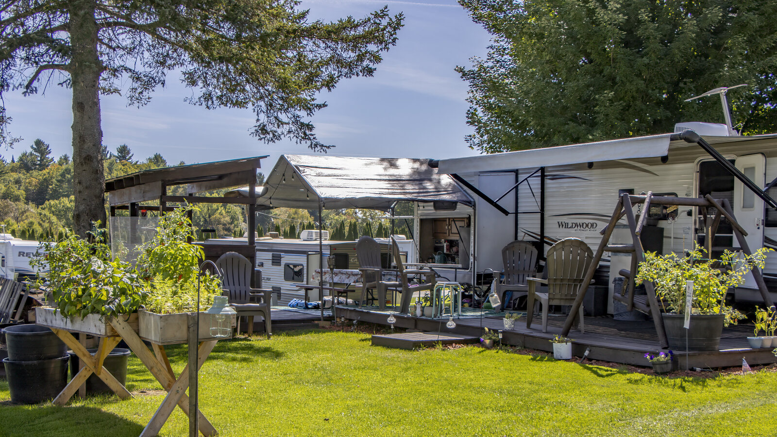 A wooded campsite with a deck, awning and outdoor seating