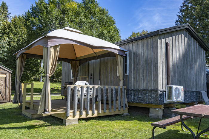 A gazebo and a picnic table beside a grey cabin with a covered deck