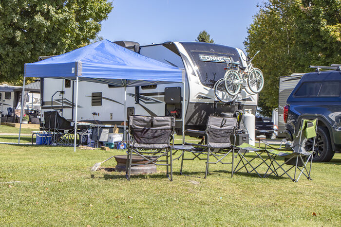 A travel trailer with a blue canopy, camp chairs and bicycles