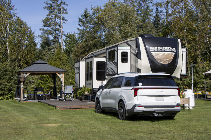 A fifth-wheel with a hardtop gazebo, a wooden deck and a car parked alongside