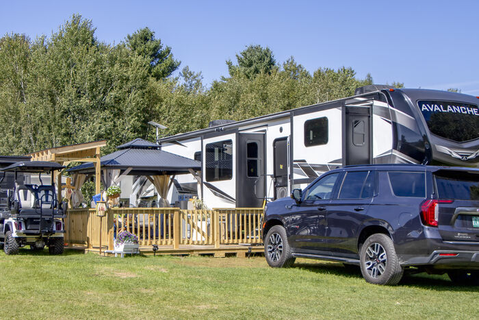 A fifth-wheel and a wooden deck backing onto the treeline