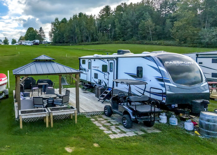 A travel trailer beside a hardtop gazebo on a wooden deck, with raised planters and a golf cart