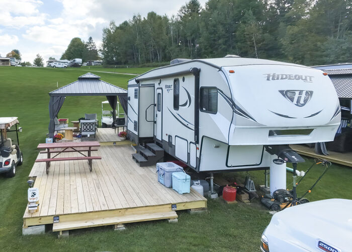A fifth-wheel with a hardtop gazebo and a picnic table on a wide wooden deck