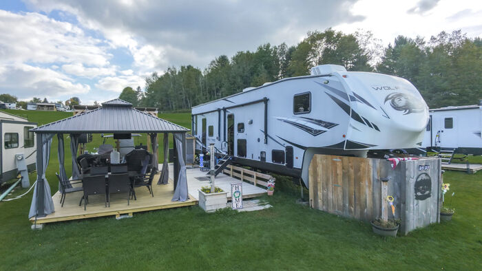 A travel trailer with a curtained hardtop gazebo, a dining set on the deck and a wooden privacy screen