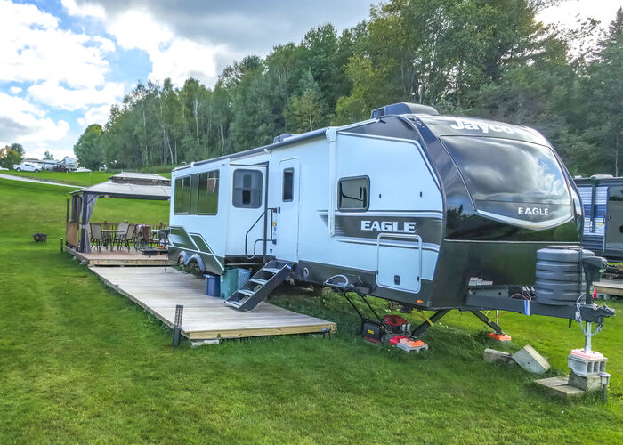 A travel trailer with a long wooden deck and steps along its side