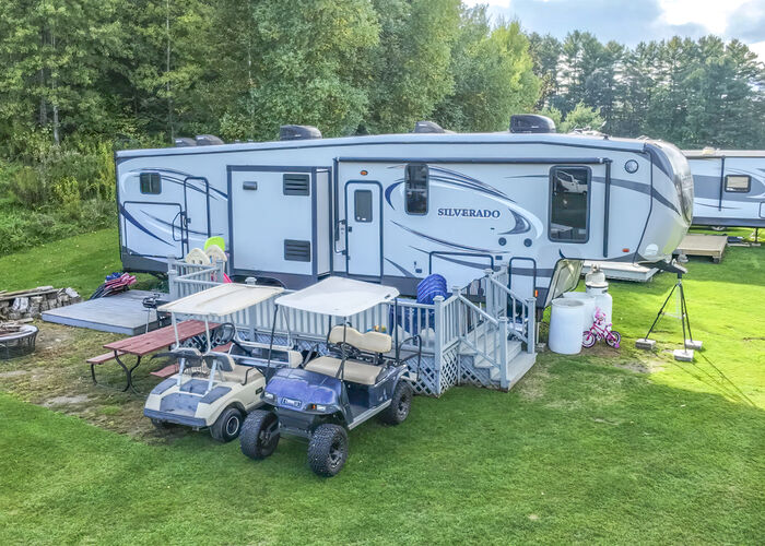 A fifth-wheel with a railed porch and lattice skirting, two golf carts and a picnic table