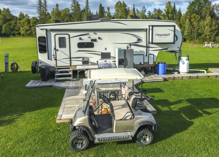 A fifth-wheel with a wooden deck and boardwalk and a golf cart parked in front