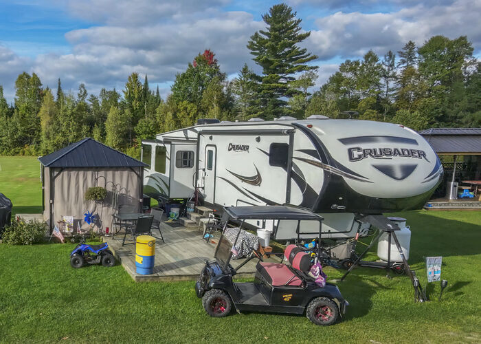 A fifth-wheel with a curtained gazebo, a deck and a golf cart parked in front