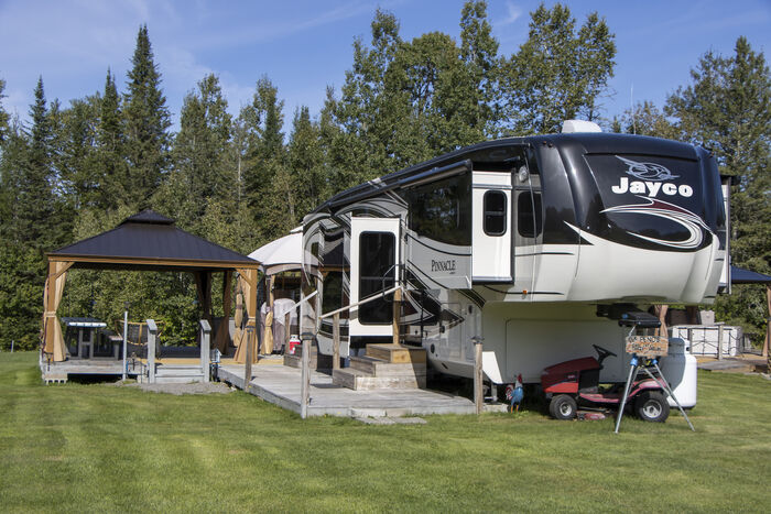 A fifth-wheel with a hardtop gazebo on a broad wooden deck, a utility vehicle parked alongside