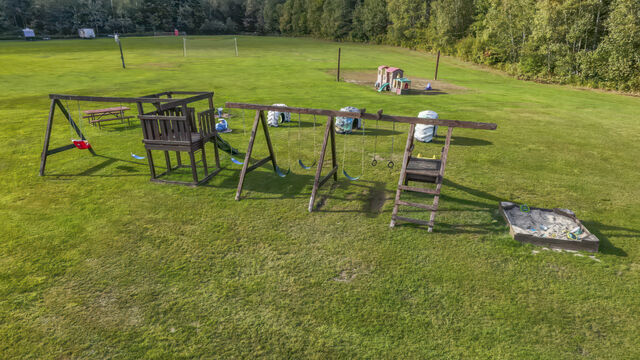 Wooden swing sets and a sandbox on an open grass field, with a small play set beyond